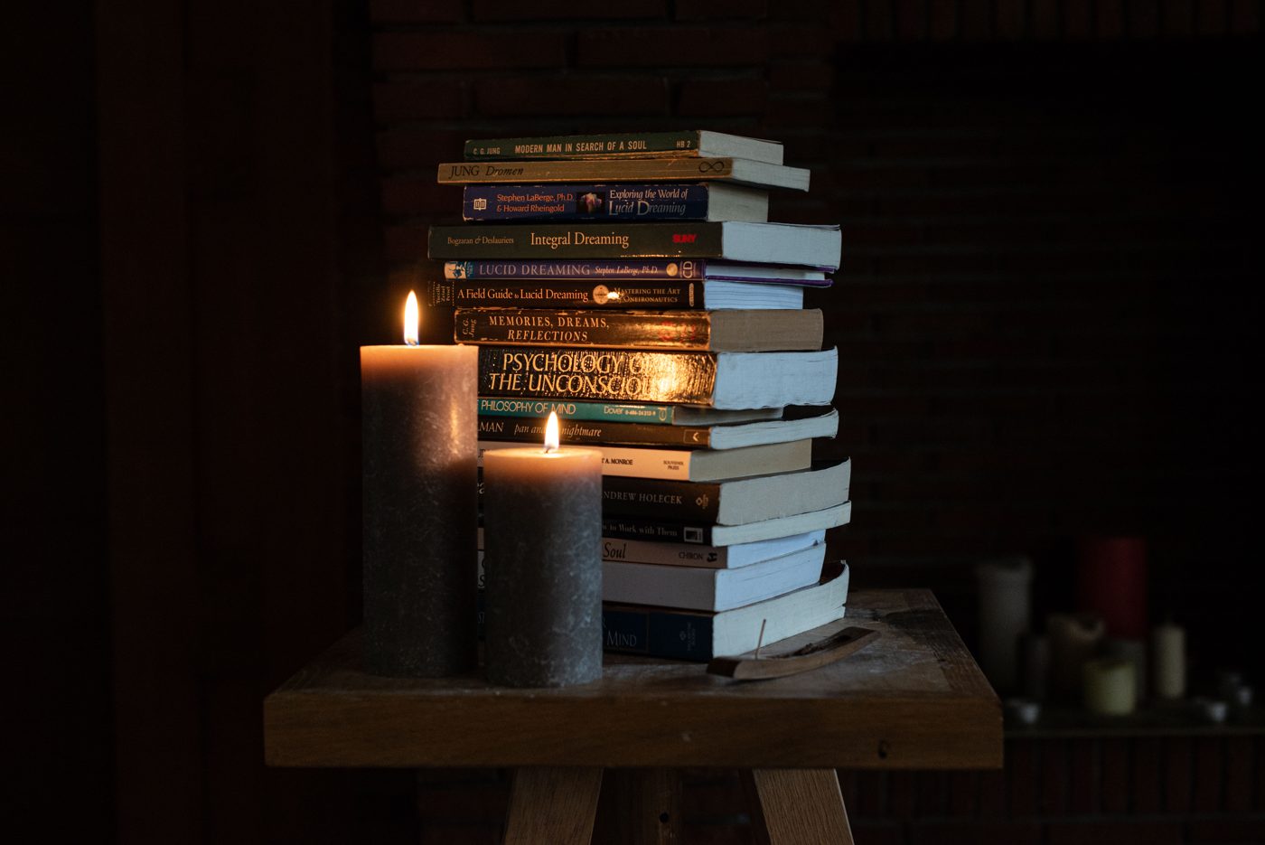 A stack of books on dreaming and the unconscious, by Jung, LaBerge and others, beside two lit candles in the dark