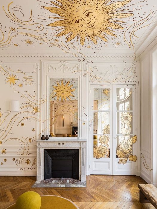 A white panelled room with a golden sun on the ceiling and a fireplace