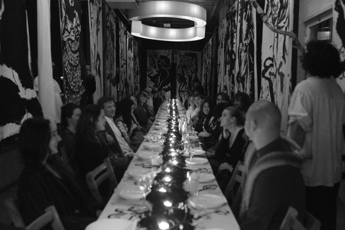 A long candlelit table in a room hung with black-and-white painted banners