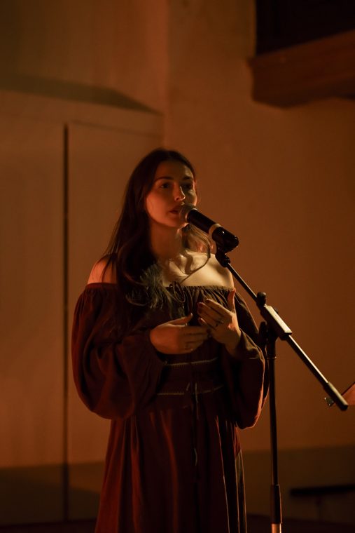 Marieke McKenna speaking into a microphone in warm amber light