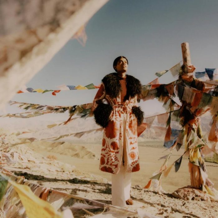 A model in an embroidered coat on a beach under prayer flags, for Zazi Vintage
